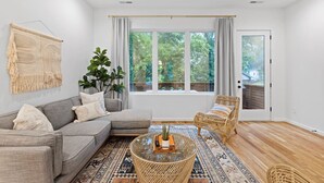 A modern living room with a grey sectional sofa, a wicker coffee table, and a large window with curtains.