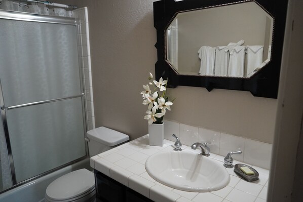 A bathroom with a shower, toilet, sink, and a mirror with a towel rack.