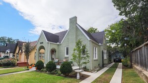 A two-story house with a front porch, a small garden, and a driveway. - Newly Restored 2BR Heights Cottage (Little Rock)