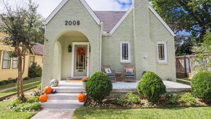 A house with the number 2008 on the front, a porch with chairs, and a well-maintained lawn with a pumpkin. - Newly Restored 2BR Heights Cottage (Little Rock)