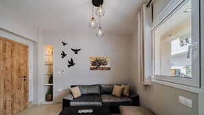 A modern living room with a sofa, a coffee table, a wooden door, a wall-mounted light fixture, and a window. - Napoleon Olive Home 2bd 1ba (Hersonissos)