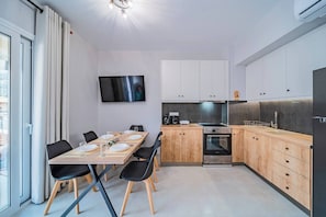 A modern kitchen with wooden cabinets, a built-in oven, and a dining area with a table set for four. - Napoleon Olive Home 2bd 1ba (Hersonissos)