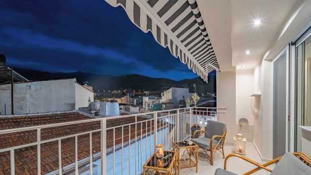 A balcony with a view of a cityscape at dusk, wicker furniture, and a white railing. - Napoleon Olive Home 2bd 1ba (Hersonissos)