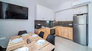 A modern kitchen with white cabinets, a stainless steel refrigerator, and a dining area with a wooden table set for four. - Napoleon Olive Home 2bd 1ba (Hersonissos)