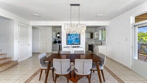 A modern dining area with a large wooden table and grey upholstered chairs, a chandelier, and a kitchen in the background. - Dos Culebras House-Private Pool (Puntas)