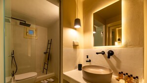 A bathroom with a toilet, a sink with a large basin, and a mirror above the sink. There are towels on the floor and a ladder leaning against the wall.