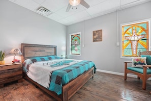 A bedroom with a wooden bed, a nightstand, a lamp, a chair, and a window with stained glass. - Historic Home Near Table Rock Lake, Branson (Omaha)