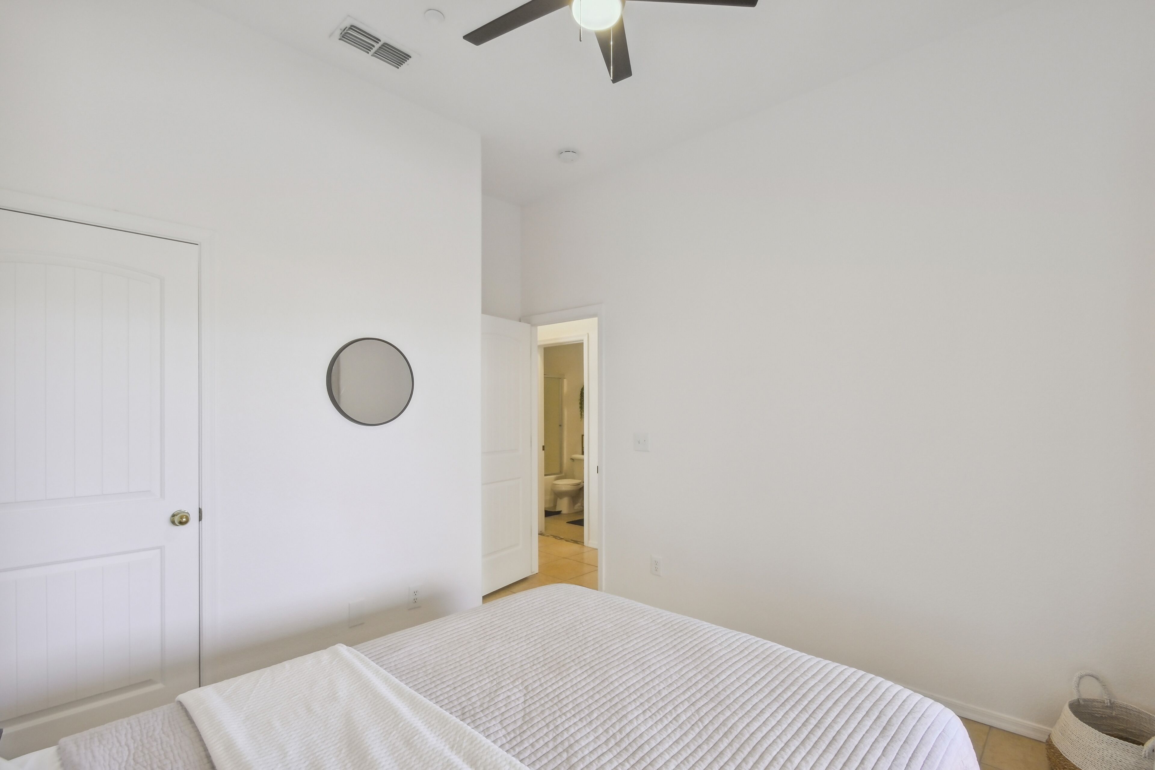 Un dormitorio con una cama, un ventilador de techo, una puerta y un pasillo que conduce a un baño.