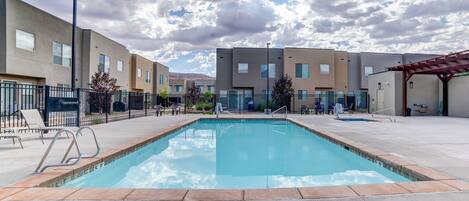 Piscina rectangular con indicador de profundidad de 1,5 metros, rodeada por una terraza pavimentada con sillas de descanso y una pérgola.
