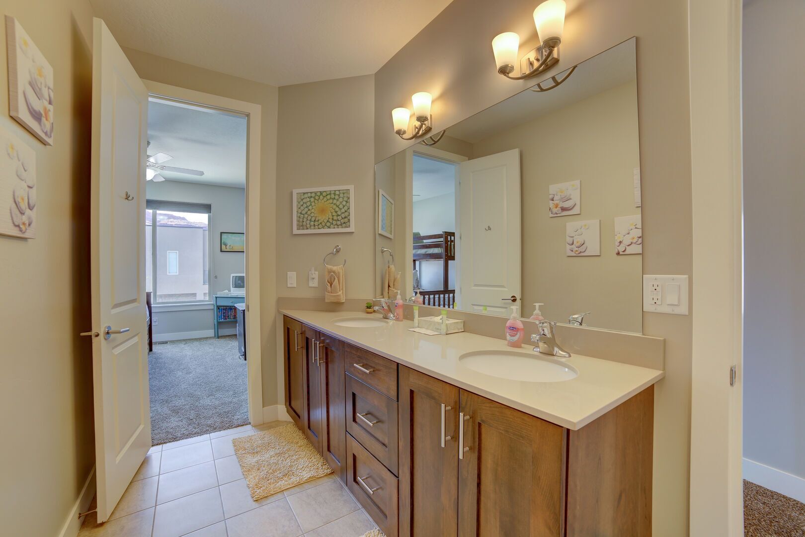 A modern bathroom with a double sink, wooden cabinets, a large mirror, and wall-mounted lighting.