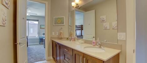A modern bathroom with a double sink, wooden cabinets, a large mirror, and wall-mounted lighting.