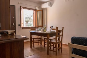 A dining area with a wooden table and chairs, a window with a view of trees, and an air conditioning unit on the wall.