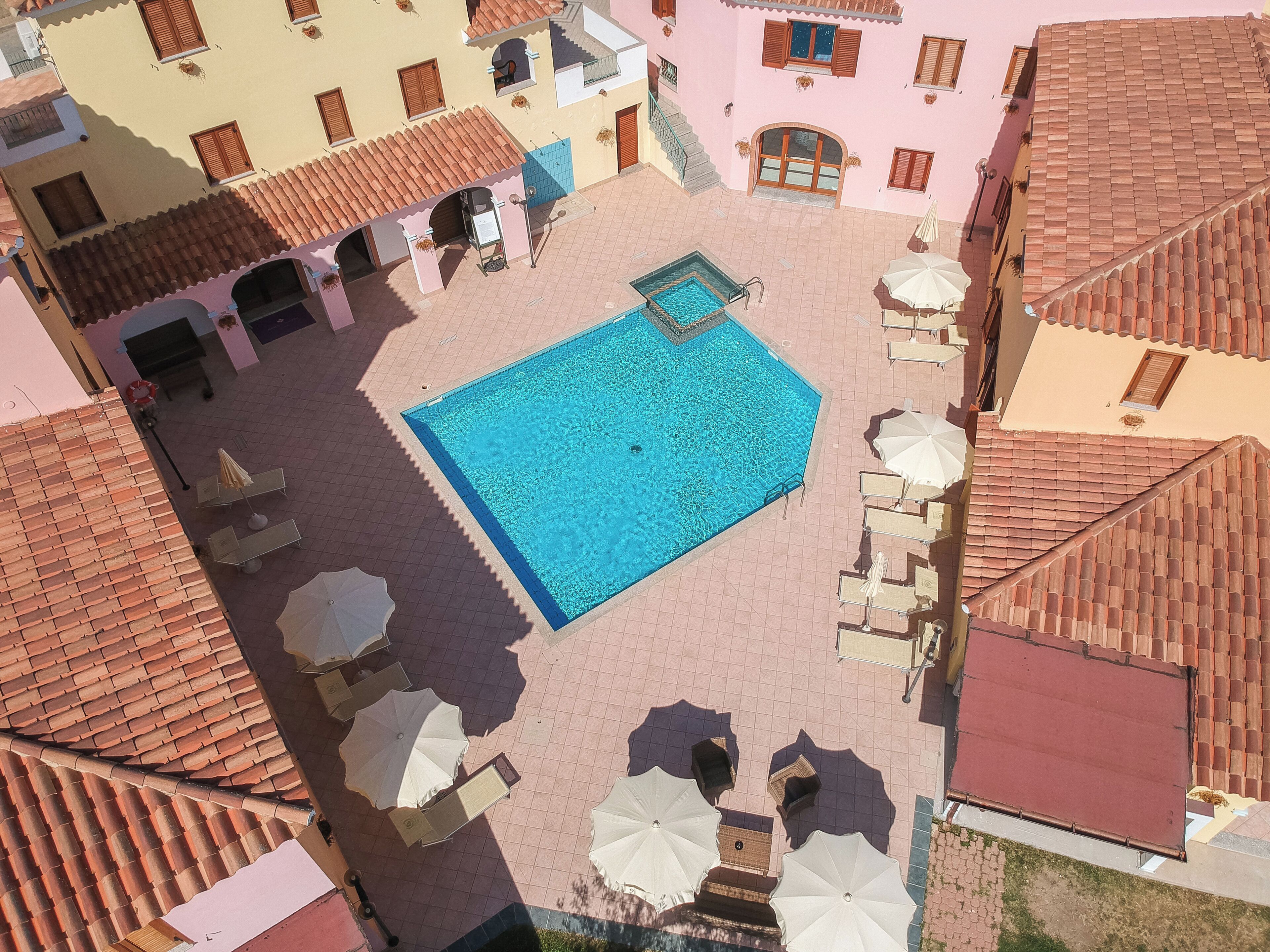 An aerial view of a courtyard with a swimming pool, surrounded by buildings with terracotta roofs and balconies.
