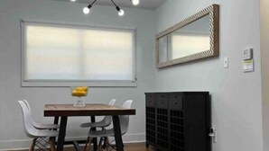 A dining area with a wooden table, white chairs, a modern chandelier, a large window, and a black cabinet. - Atlanta Home - 10 min from everything! (Atlanta)