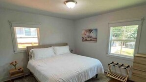 A bedroom with a large bed, a wooden dresser, a nightstand, a rug, and two windows. - Atlanta Home - 10 min from everything! (Atlanta)