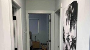 A narrow hallway with wooden flooring, white walls, and a painting of palm trees. - Atlanta Home - 10 min from everything! (Atlanta)