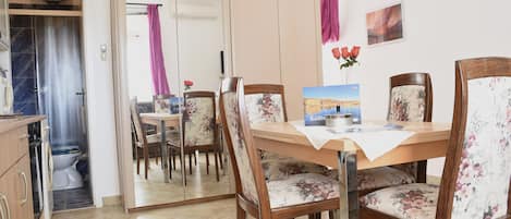 A dining area with a wooden table, floral chairs, and a view of the bathroom through a sliding door.