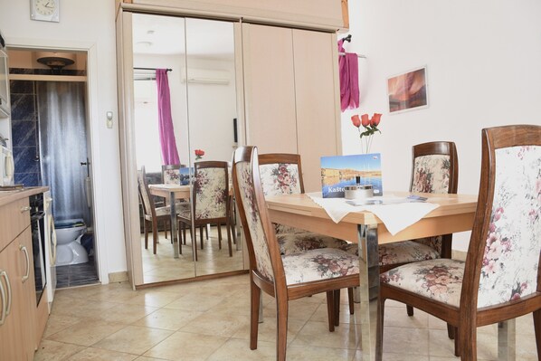 A dining area with a wooden table, floral chairs, and a view of the bathroom through a sliding door.