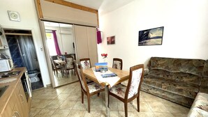 A dining area with a wooden table and chairs, a sofa, and a kitchen area with cabinets and a microwave.