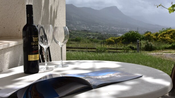 A table with a wine bottle and glasses, an open magazine, and a view of a mountainous landscape.