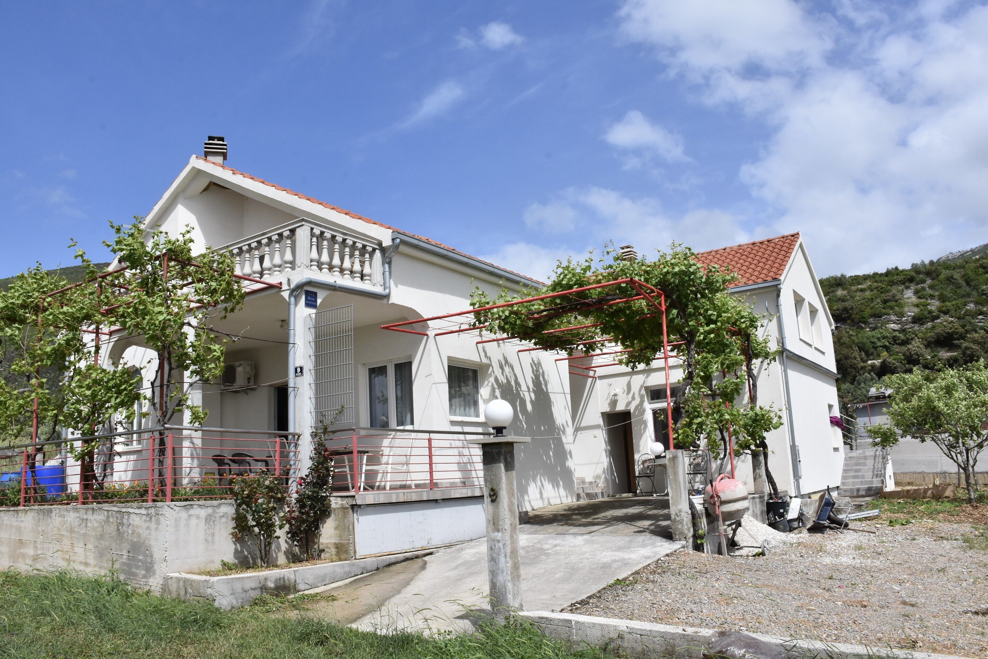 A two-story building with a red-tiled roof, a balcony, and a small garden area.