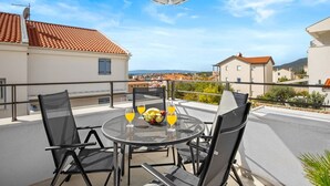 A balcony with a round table, two chairs, and a bowl of fruit and drinks. - Apartment Tim (Cres)