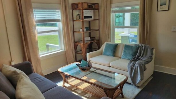 Ein Wohnzimmer mit einer Couch, einem Glastisch, einem Bücherregal und Blick ins Freie.