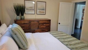 Ein Schlafzimmer mit einem Bett, einer Kommode, zwei gerahmten Bildern und einer Tür zu einem anderen Raum.