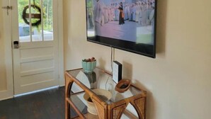 Ein an der Wand befestigter Fernseher mit einem Glastisch davor, der eine Szene von Personen in weißer Kleidung zeigt.