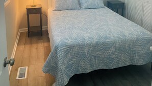 A bedroom with a bed, a nightstand with a lamp, a ceiling fan, a window with blinds, and a wardrobe.