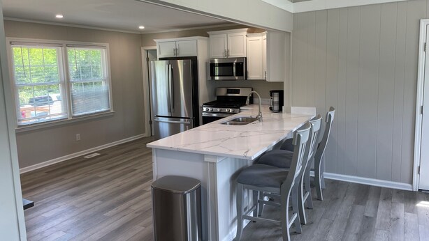 A modern kitchen with a marble countertop, stainless steel appliances, and a bar area with bar stools.