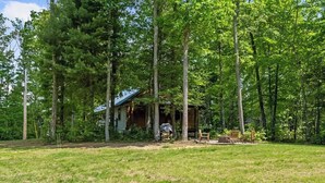 Eine rustikale Holzhütte, umgeben von hohen Bäumen in einer grasbewachsenen Gegend.