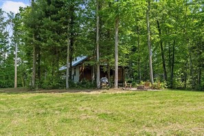 A rustic cabin surrounded by tall trees in a grassy area.