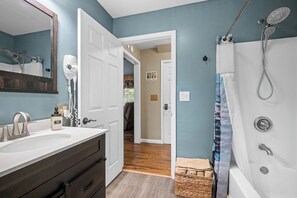 Ein Badezimmer mit einer weißen Badewanne, einer Dusche, einem großen Spiegel und einer weißen Tür zu einem anderen Raum.