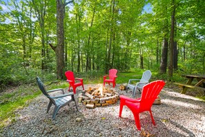 A campsite with a fire pit surrounded by Adirondack chairs, set in a forested area. - The Aspen Cabin | Hocking Hills, Charming, Hot Tub (Rockbridge)