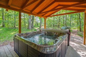 A hot tub under a wooden pergola in a forested area.