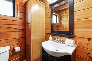 A wooden cabin bathroom with a white sink, a mirror, and a toilet.
