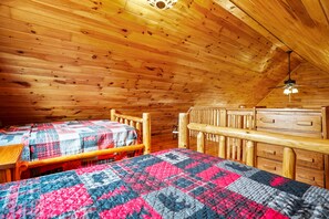 A cabin with two wooden beds, a wooden dresser, and a ceiling fan.