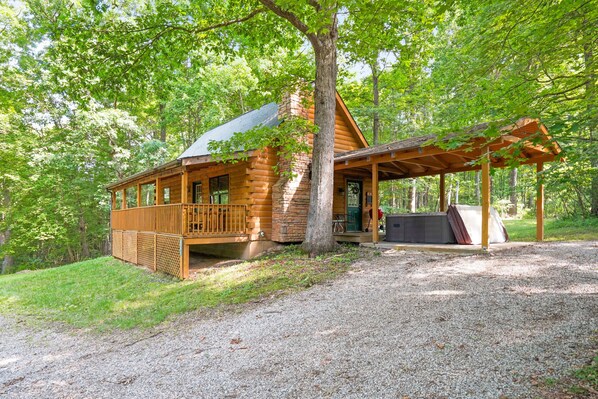 A log cabin with a porch and a covered outdoor seating area, surrounded by trees.