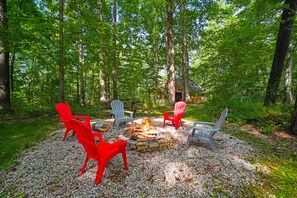 A forested area with a fire pit surrounded by red and gray Adirondack chairs. - The Aspen Cabin | Hocking Hills, Charming, Hot Tub (Rockbridge)