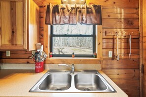 A kitchen with a double sink, wooden cabinets, and a window with a view of trees.