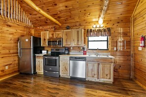 A wooden cabin kitchen with a refrigerator, microwave, stove, and dishwasher.
