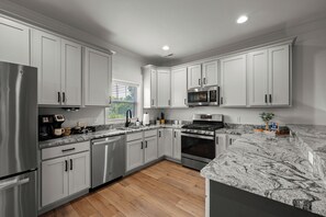 A modern kitchen with white cabinets, stainless steel appliances, and a marble countertop.