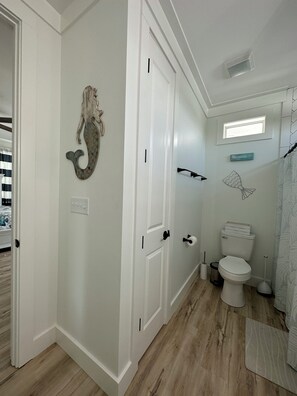 A bathroom with a white toilet, a shower curtain, a wall-mounted towel rack, and a decorative fish sculpture. - PCB FUN-heated pool, hot tub, golf cart, putt putt (Panama City Beach)