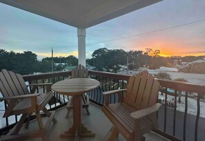 A balcony with wooden chairs and a table, overlooking a residential area during sunset. - PCB FUN-heated pool, hot tub, golf cart, putt putt (Panama City Beach)