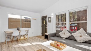 Un salon moderne avec un canapé gris, une table basse blanche et un coin repas comprenant une table et des chaises en bois.