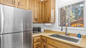 Une cuisine dotée de meubles en bois, d’appareils électroménagers en acier inoxydable, d’un four à micro-ondes encastré et d’une grande fenêtre offrant une vue sur les arbres.