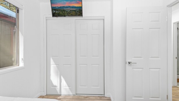 Un couloir avec deux portes blanches, un tableau au-dessus de la porte de gauche et une fenêtre sur le côté gauche.