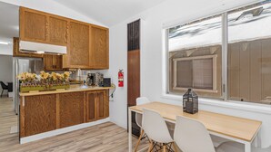 Une cuisine moderne avec des meubles en bois, une table à manger en bois entourée de chaises blanches et une fenêtre donnant sur un paysage enneigé.