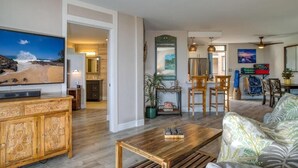 Uma sala de estar ampla com uma grande TV de tela plana, móveis de madeira e um espaço de jantar com cadeiras e mesa.